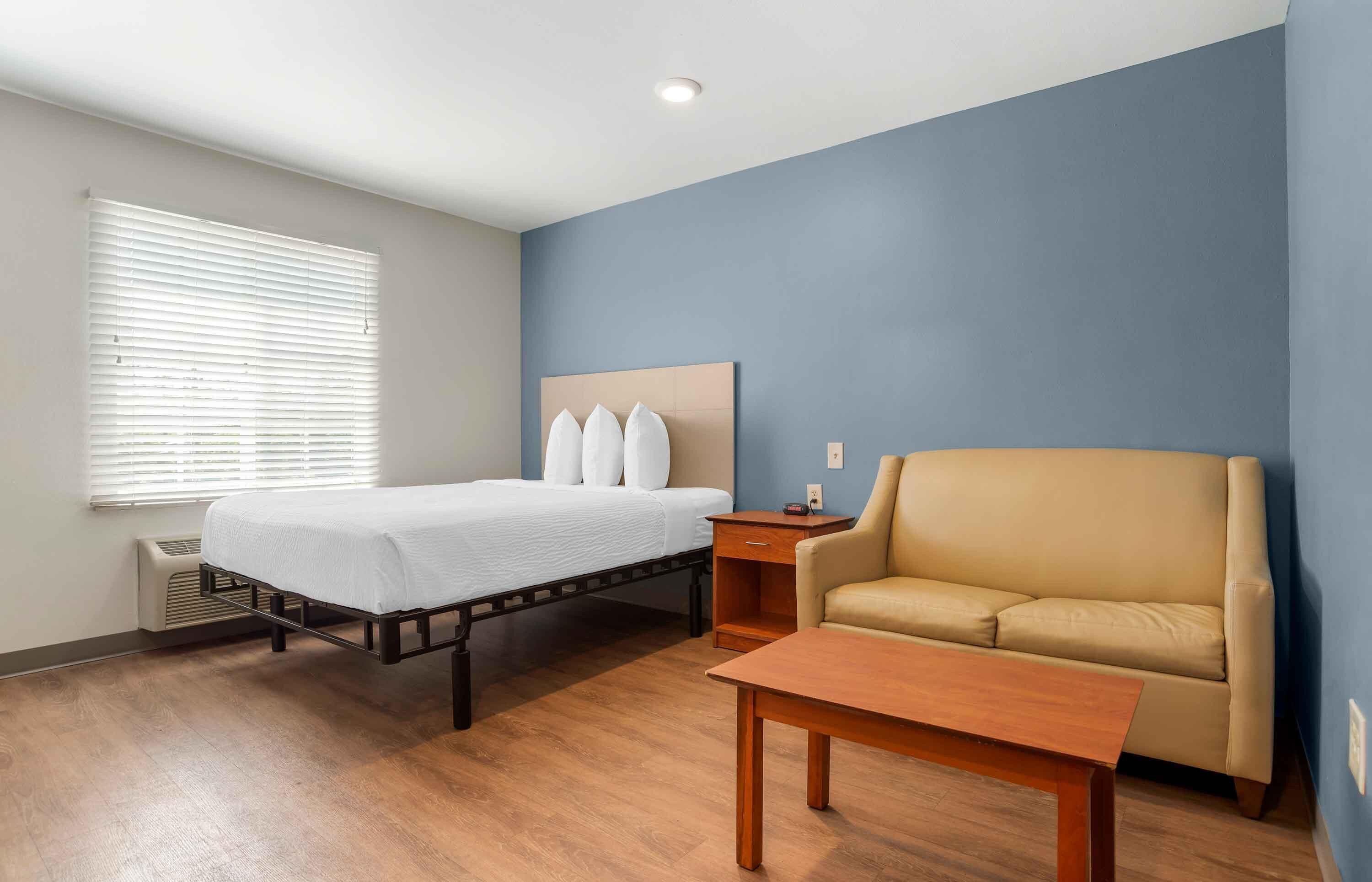 A hotel room with a bed, a sofa, a nightstand, and a wooden table.