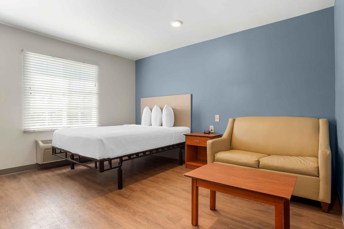 A hotel room with a bed, a sofa, a nightstand, and a wooden table.