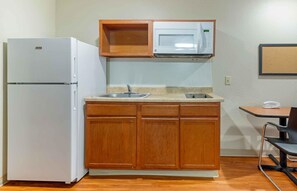 A compact kitchen with a white refrigerator, a microwave, wooden cabinets, a sink, and a small table with chairs. - Extended Stay America Select Suites - Atlanta - Chamblee (Chamblee)