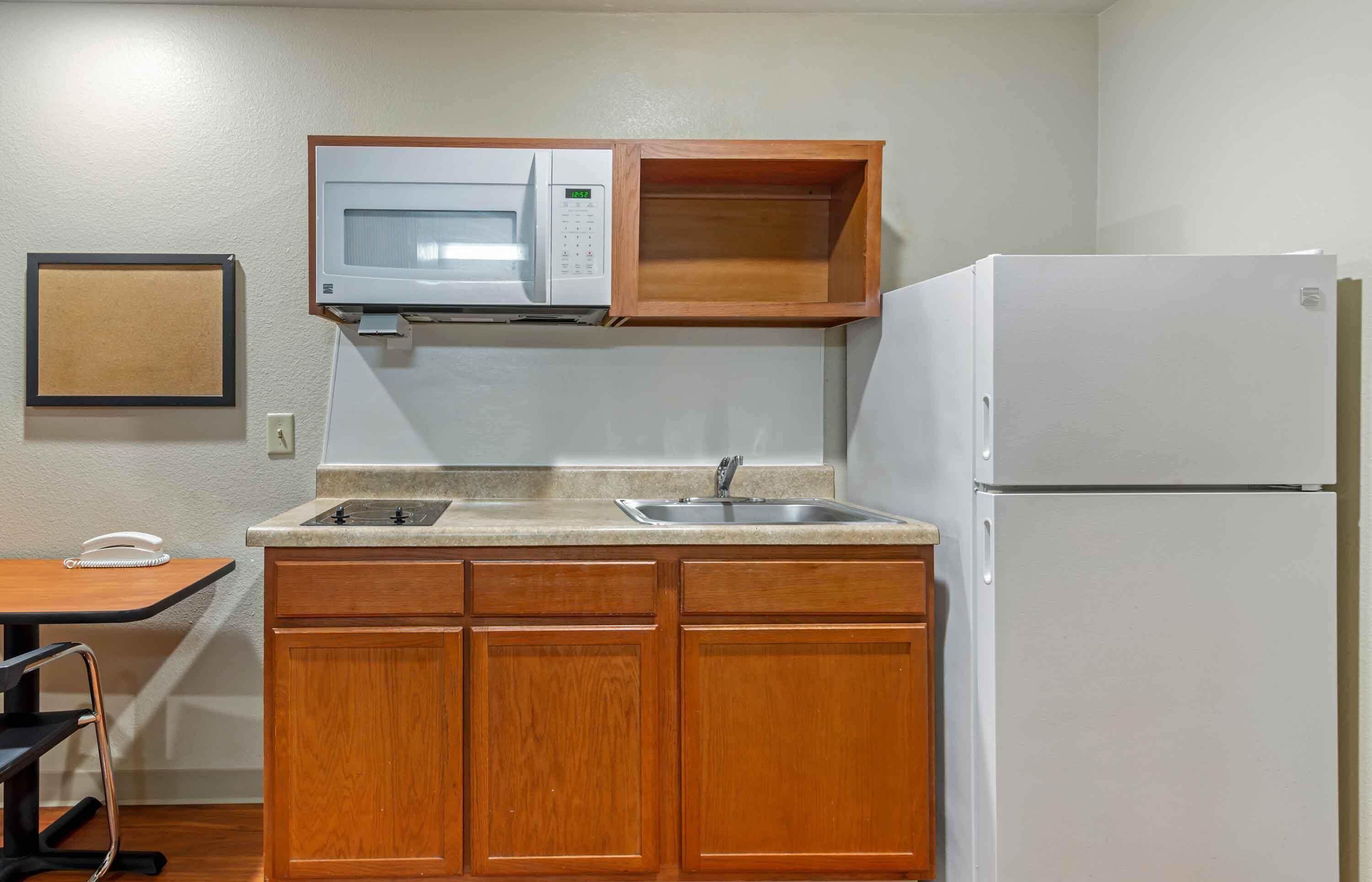 A compact kitchenette with wooden cabinets, a microwave, a sink, and a refrigerator.