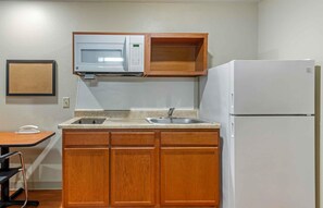 A compact kitchenette with wooden cabinets, a microwave, a sink, and a refrigerator. - Extended Stay America Select Suites - Atlanta - Chamblee (Chamblee)