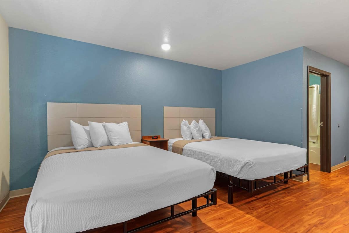 A hotel room with two beds, wooden flooring, and blue walls.