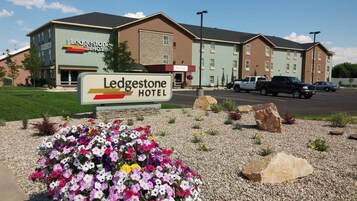 The exterior of the Ledgestone Hotel with a 'Now Open' sign, a parking lot, and a flower bed in the foreground.