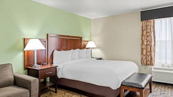 A hotel room with a bed, two bedside tables with lamps, a chair, a bench, and a patterned carpet.