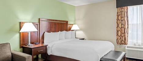 A hotel room with a bed, two bedside tables with lamps, a chair, a bench, and a patterned carpet.