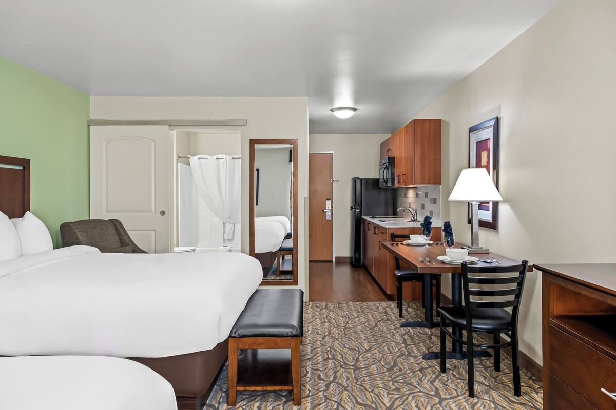 Ein Hotelzimmer mit Bett, Schreibtisch, Stuhl, Badezimmer mit Dusche und einer Küchenzeile.