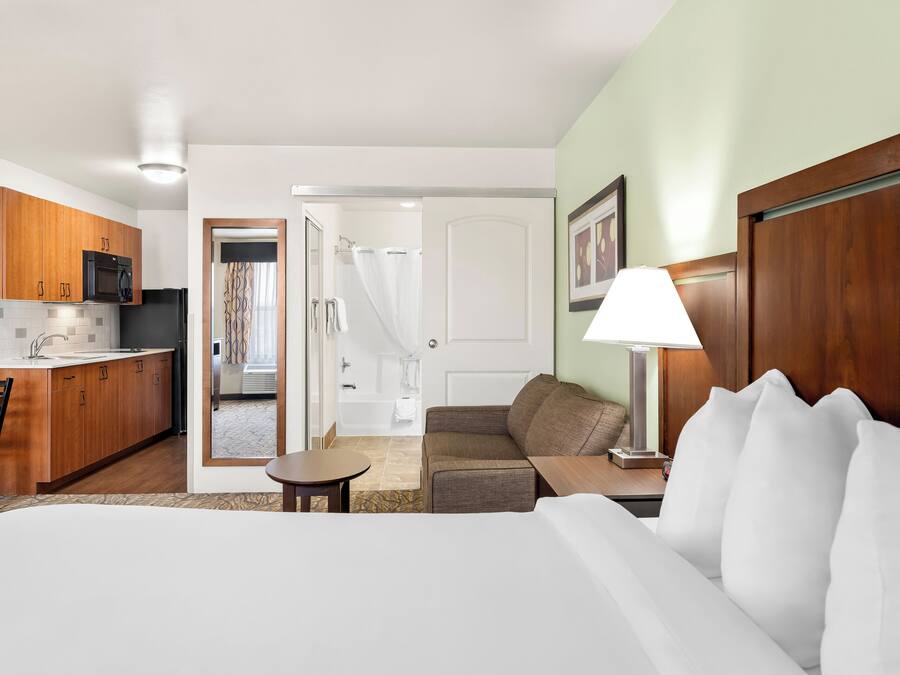 A hotel room with a bed, a small table, a sofa, a lamp, and a kitchenette with a microwave and refrigerator.