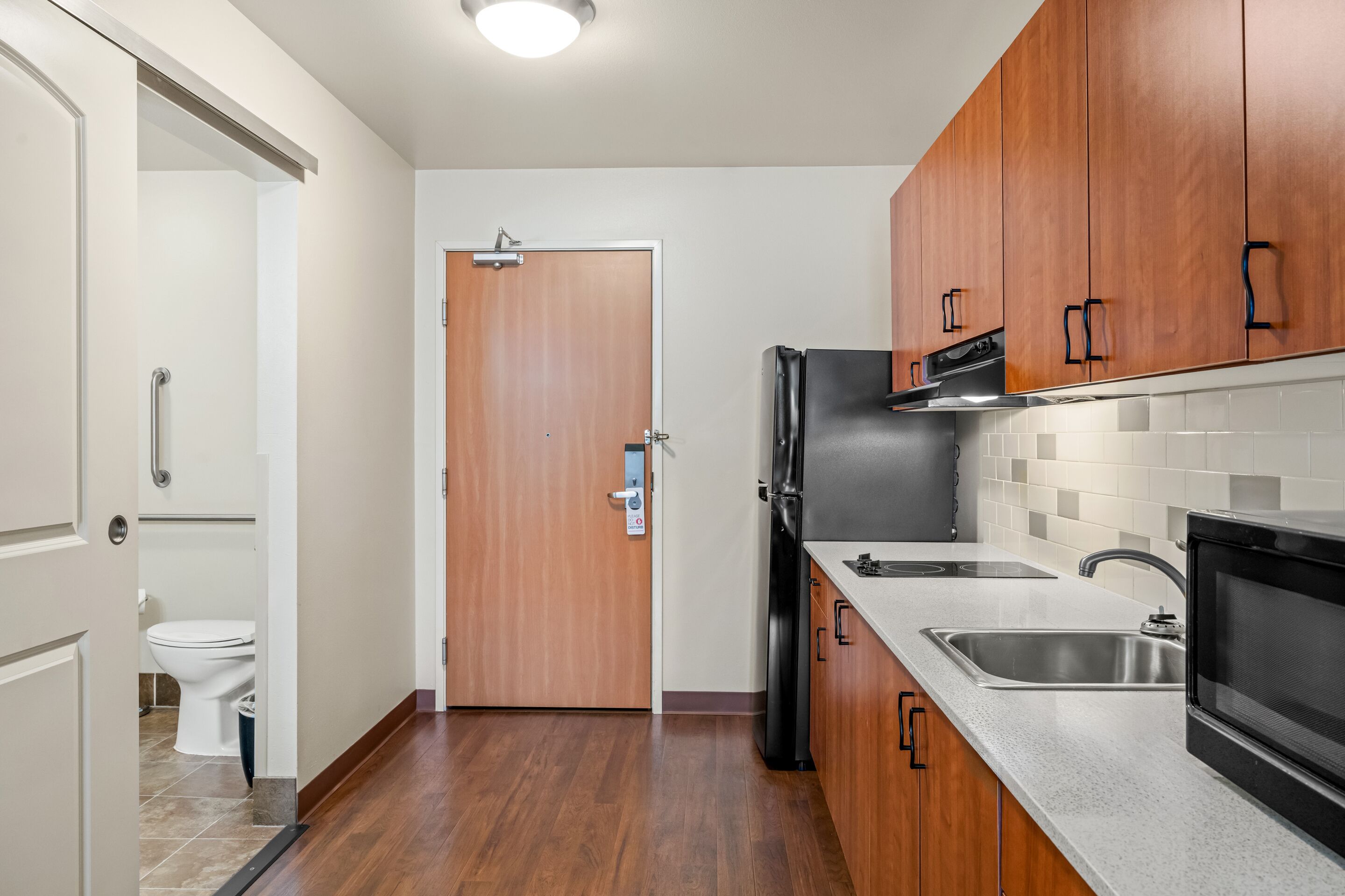 A kitchen with wooden cabinets, a refrigerator, a microwave, and a sink.