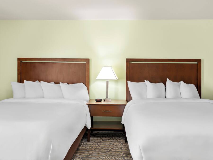 A hotel room with two beds, a nightstand with a lamp, and a small drawer.