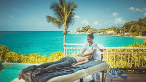 Een massage therapie sessie op een houten terras met uitzicht op een turquoise zee en een palmboom.
