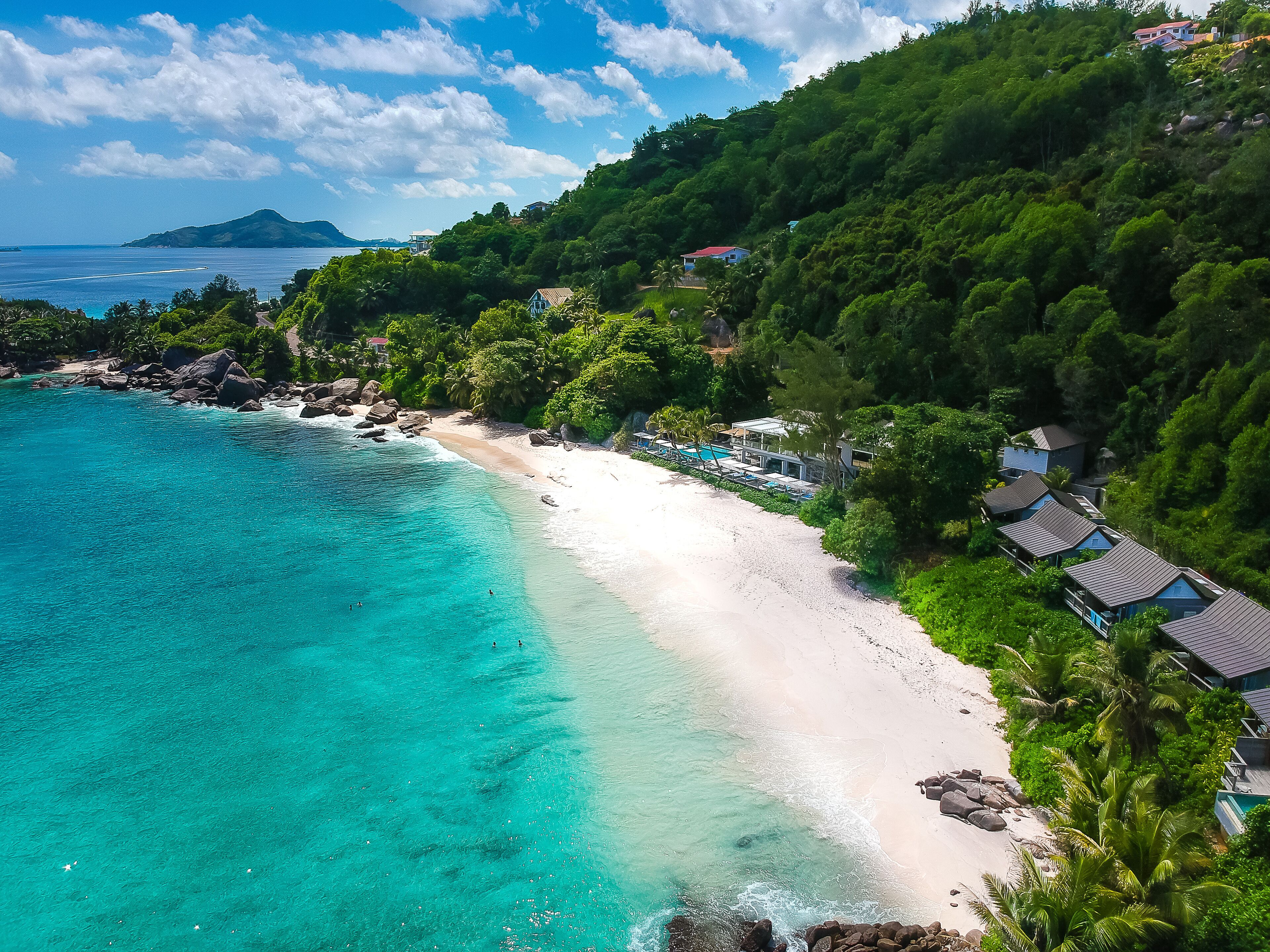 Un complejo turístico frente al mar con playa, aguas turquesas cristalinas y abundante vegetación.