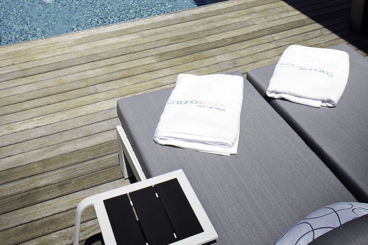 Ein Poolbereich mit Liegestühlen und einem Tablet, mit Blick auf einen Strand und das Meer.