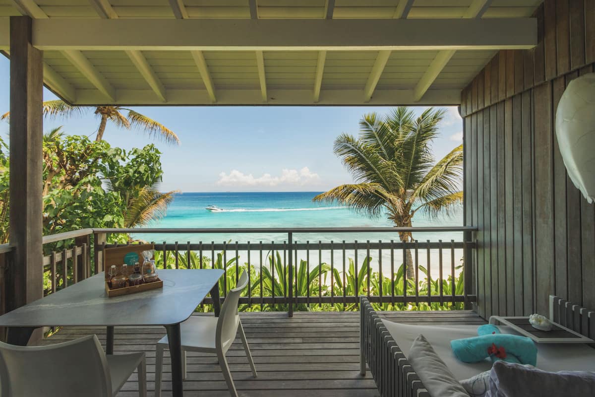 Ein überdachter Außenbereich mit Blick auf das Meer, ein Tisch mit Stühlen und eine Couch mit Kissen.