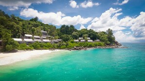 Um resort à beira-mar com bangalôs sobre a água, uma praia de areia e águas azul-turquesa.