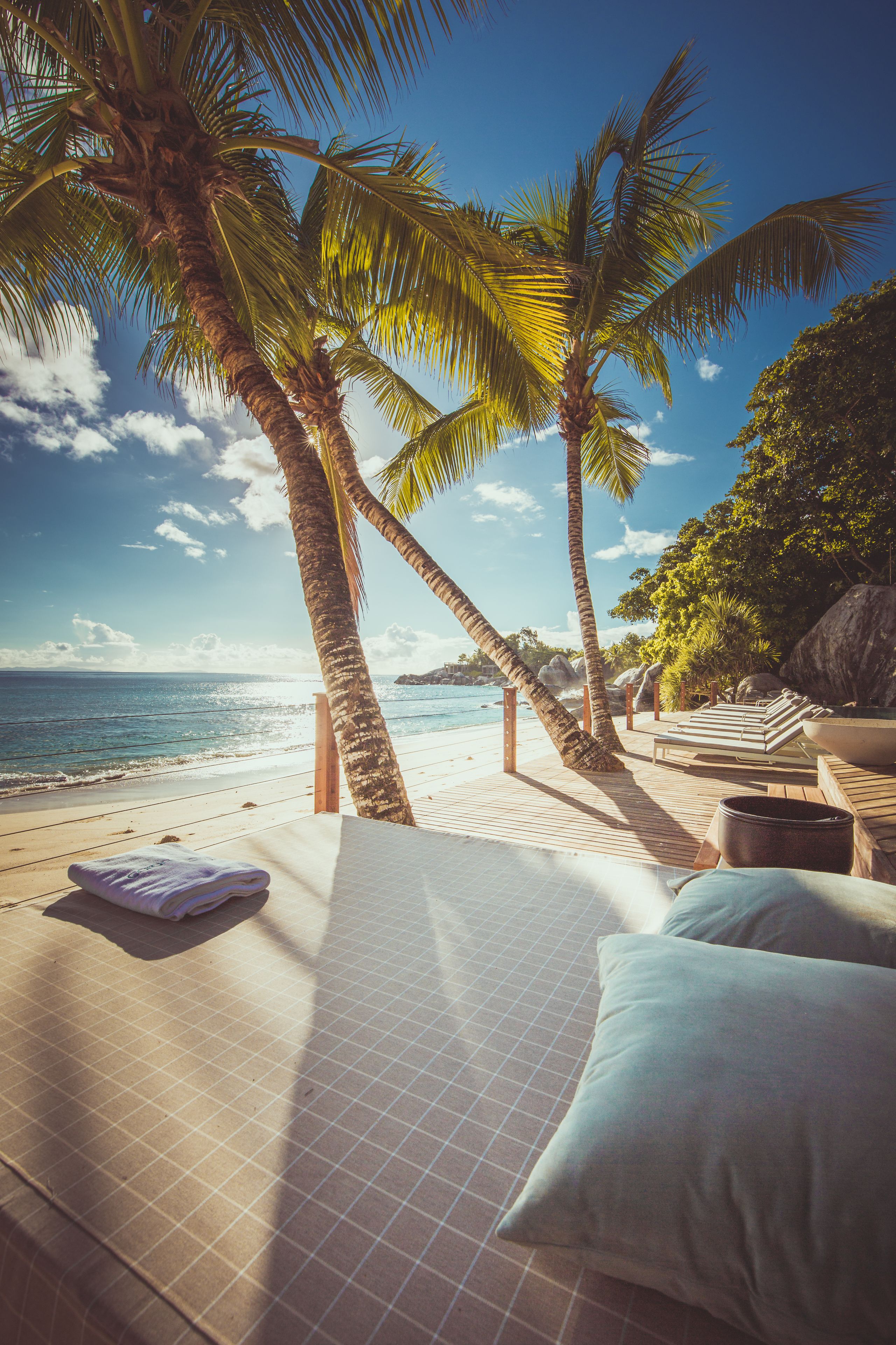 Een hotelkamer aan het strand met een bed, kussens en uitzicht op de oceaan en palmbomen.