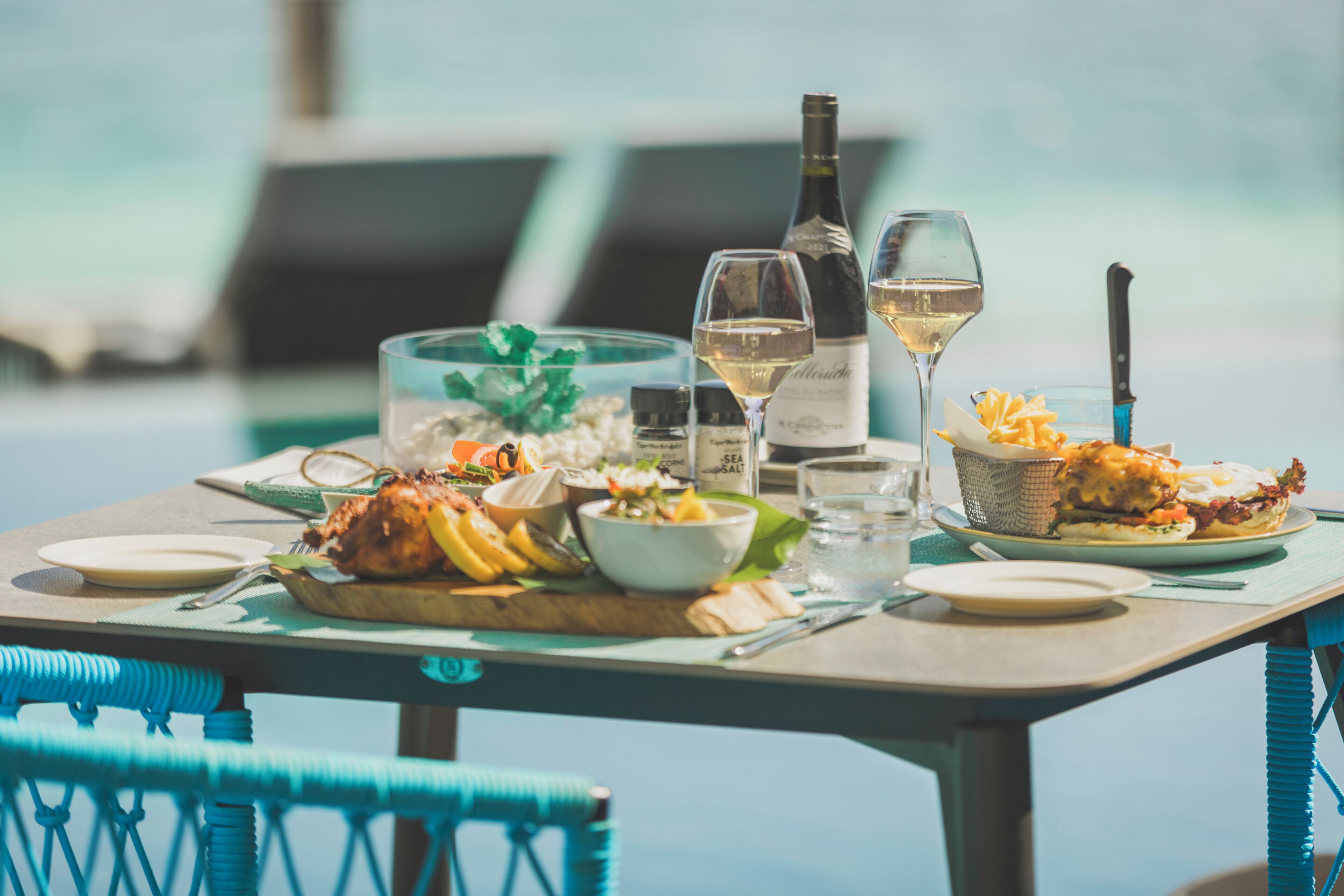 A dining table with food, wine, and a view of the sea.
