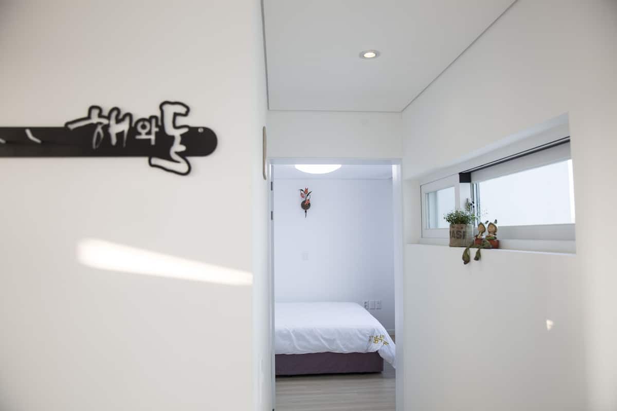 A modern bedroom with a bed, a window with a view, and a wall-mounted shelf with decorative items.