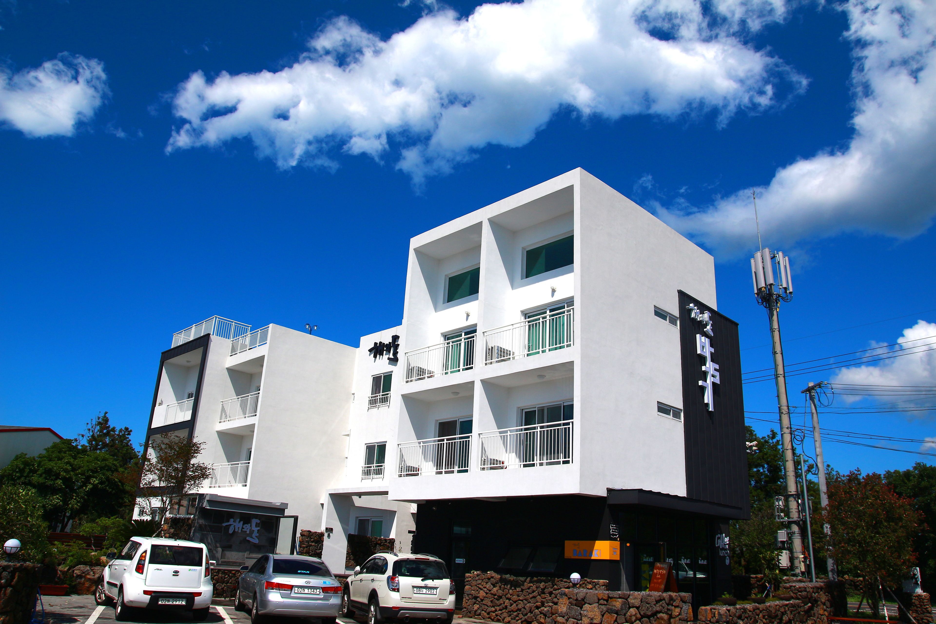Um edifício de vários andares com varandas, área de estacionamento e uma placa indicando um estabelecimento comercial.