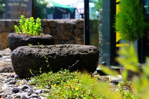 A stone planter with greenery, a stone wall, and a glass door in the background. - Jeju Baraki (Seogwipo)