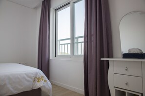 Une chambre à coucher avec un lit, une commode, un miroir et une fenêtre avec des rideaux.
