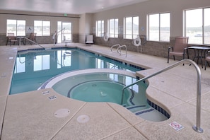Un espace piscine d’hôtel comprenant un jacuzzi, des chaises longues et un panneau indiquant la présence d’un sauveteur.