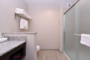 Une petite salle de bain dotée d’un plan de toilette en granit, de toilettes et d’une cabine de douche en verre.