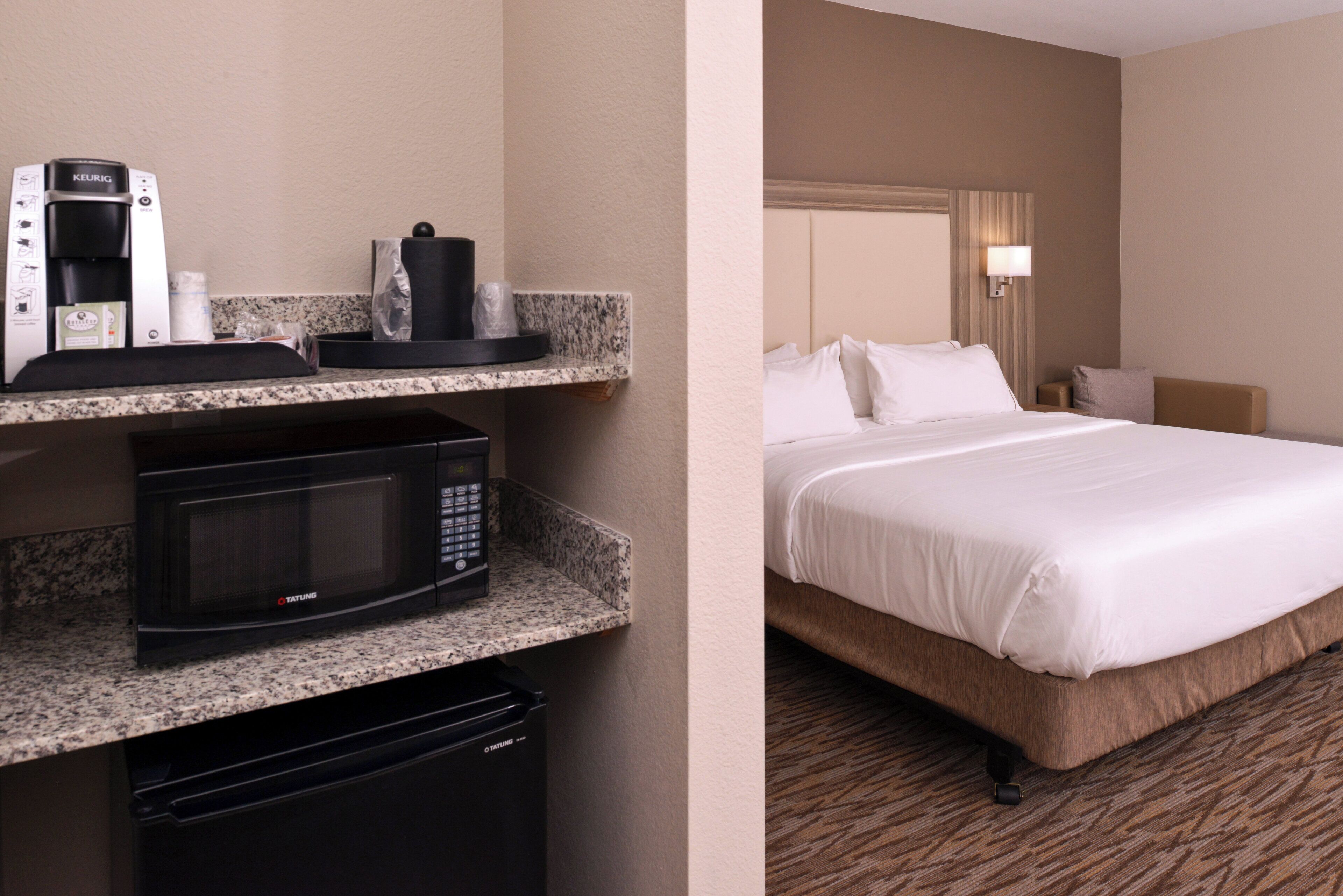 A hotel room with a bed, a minibar, a coffee maker, and a microwave.