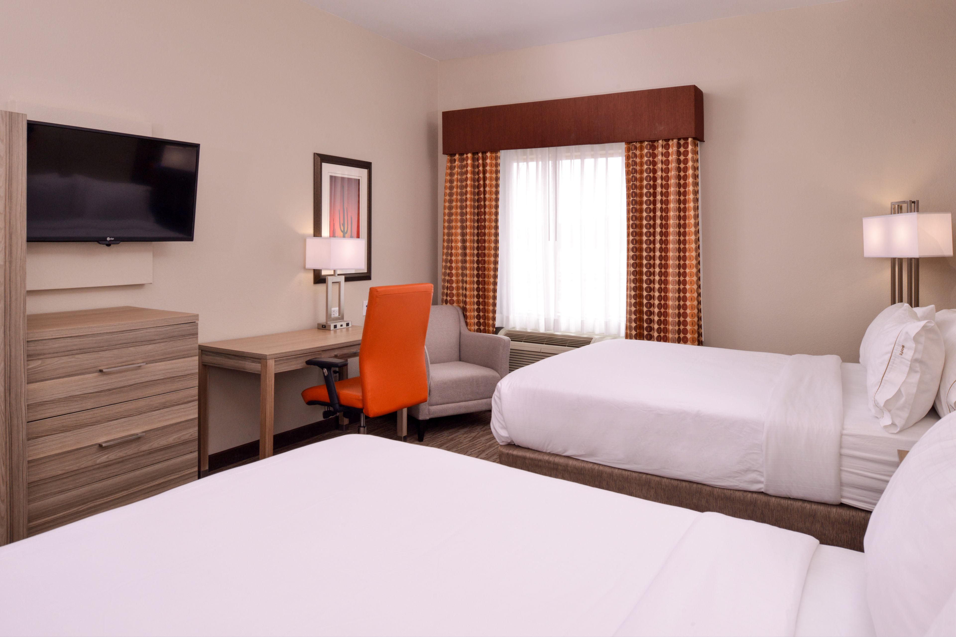 A hotel room with two beds, a desk, a chair, a TV, and a window with curtains.