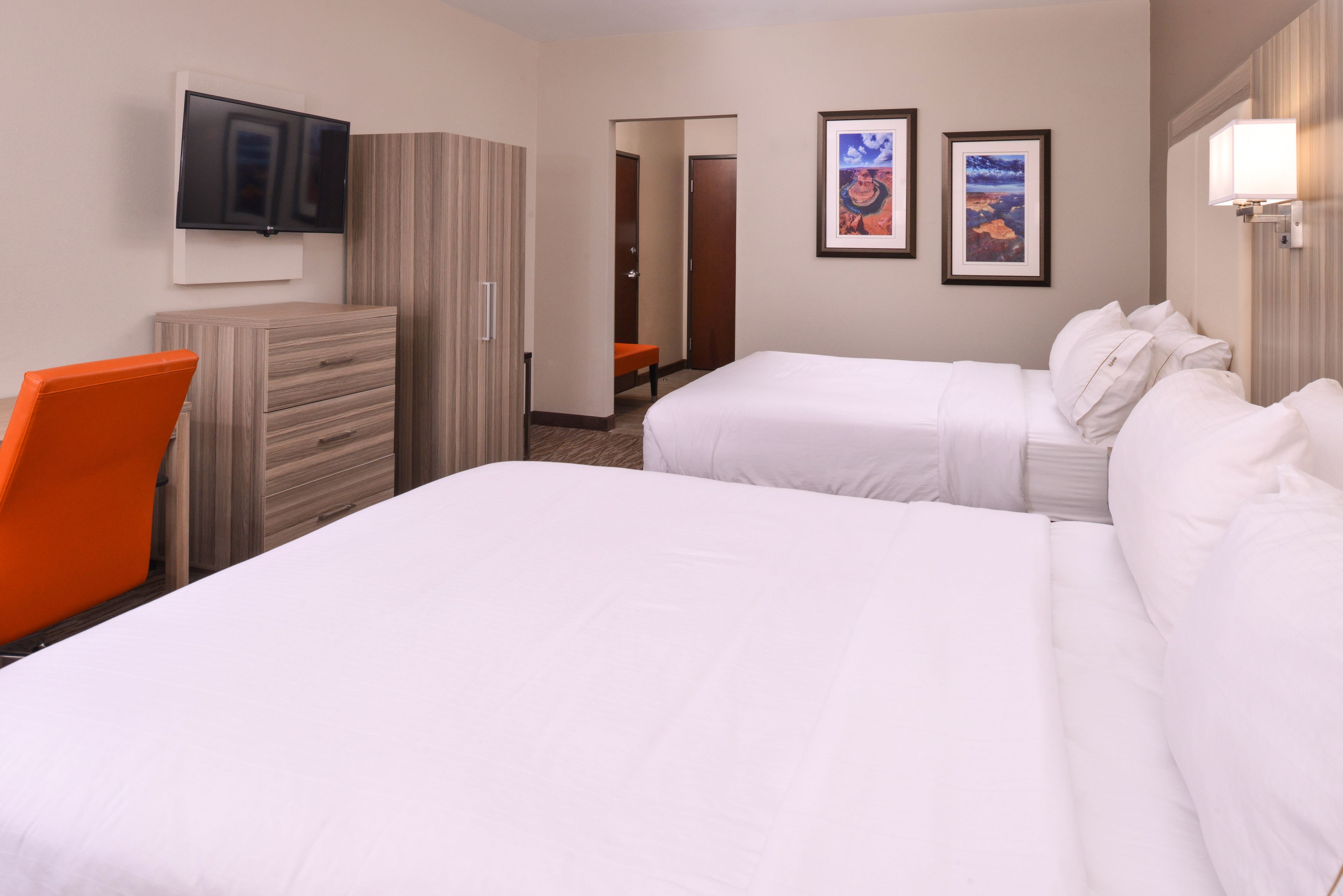 A hotel room with two beds, a television mounted on the wall, and a desk with an orange chair.