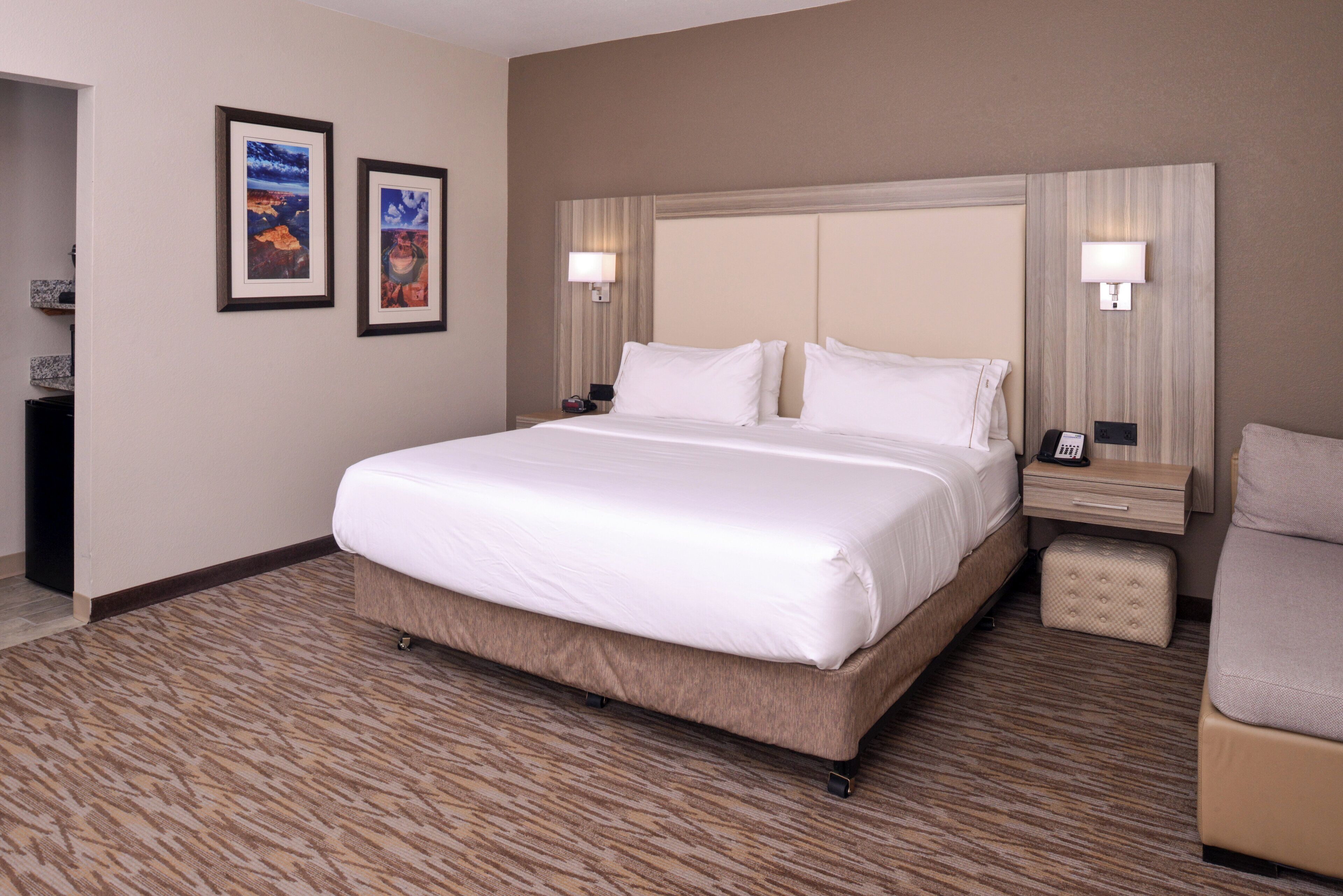 A hotel room with a large bed, two bedside tables, a nightstand, a chair, and two framed pictures on the wall.