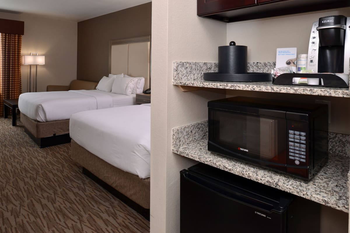 A hotel room with two beds, a microwave, a coffee maker, and a minibar.