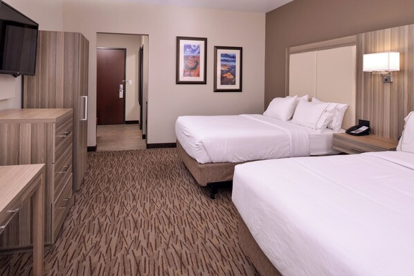 A hotel room with two beds, a desk, a television, framed pictures on the wall, and a carpeted floor.