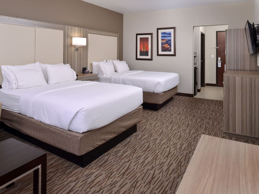 A hotel room with two beds, a sofa, a TV, and a desk.