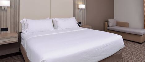 Habitación de hotel con una cama grande, mesitas de noche, un sofá y lámparas fijadas a la pared.
