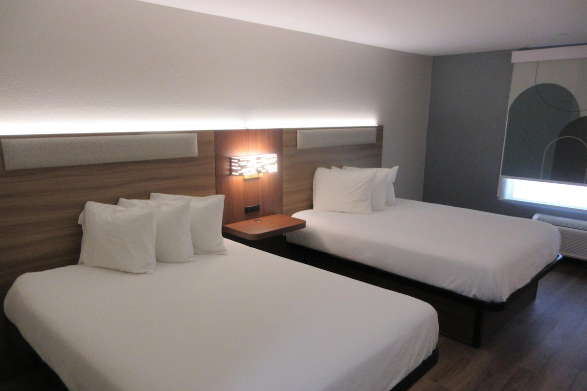 A hotel room with two single beds, a nightstand with a lamp, and a window with a view.