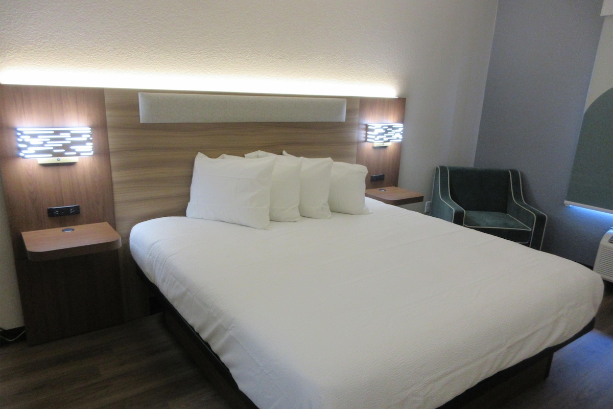 A hotel room with a large bed, two bedside tables, a chair, and a wall-mounted light fixture.