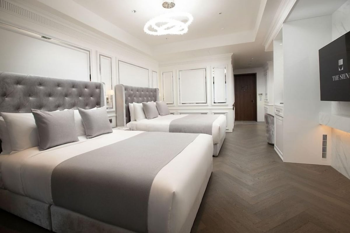 A hotel room with two large beds, a chandelier, a flat-screen TV, and a wooden floor.