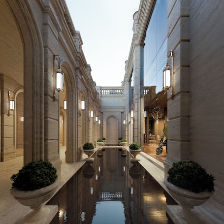 A grand hallway with a reflective pool, flanked by columns and ornate lighting fixtures.