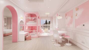 Quarto infantil em tons de rosa, com beliches, espaço de recreação e mesa de jantar com cadeiras.