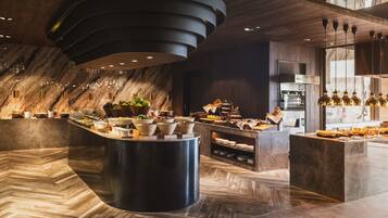 A modern hotel lobby with a marble reception desk, a large central island with food and drink options, and a stylish ceiling design.