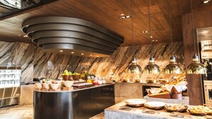 A modern breakfast bar with marble walls, a central island with food and drinks, and pendant lighting. - The Siena PRIMO (Seogwipo)