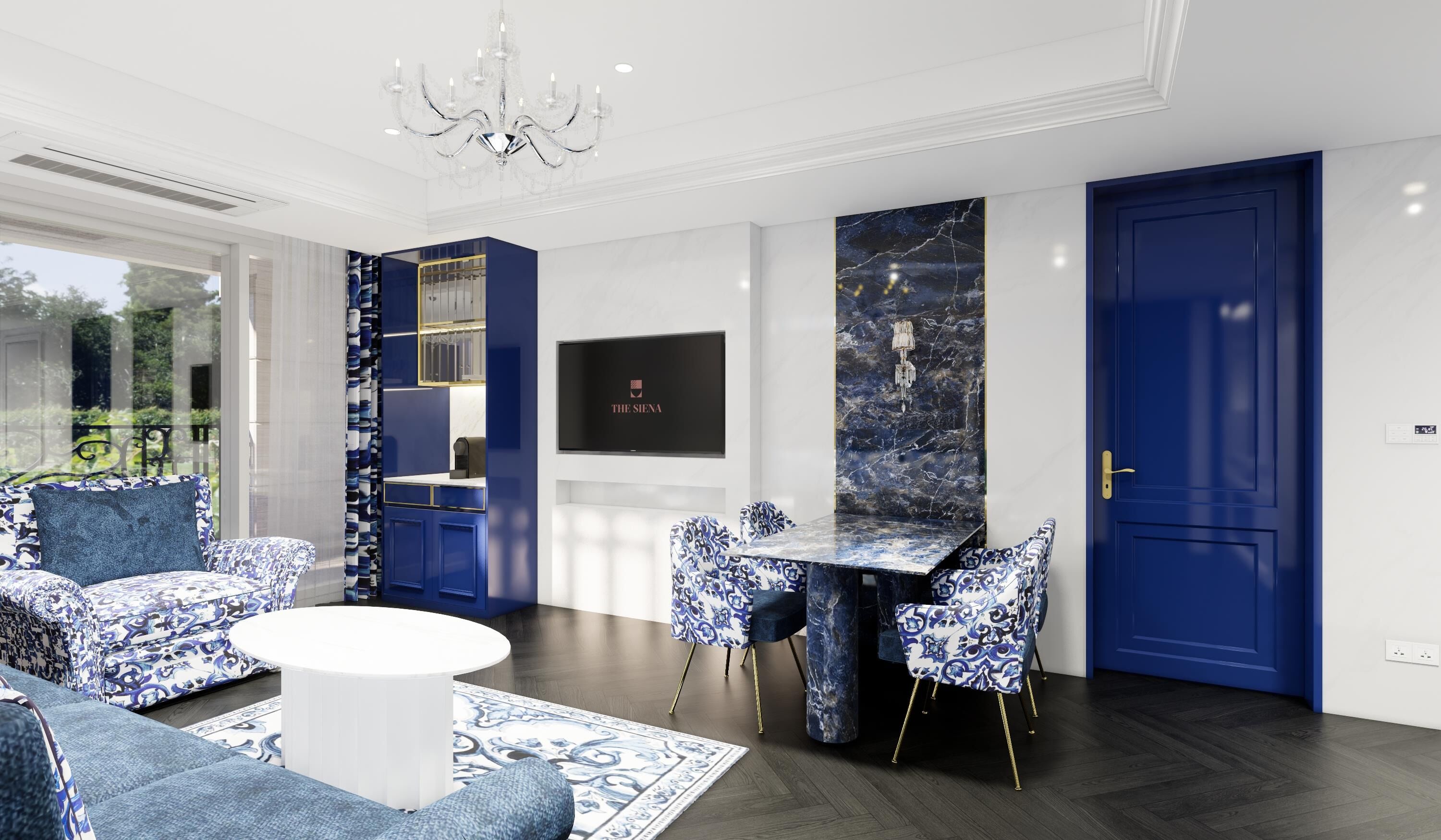 A modern living room with a round white coffee table, blue patterned sofas, and matching chairs. There is a dining area with a marble table and chairs, a chandelier, and a TV mounted on the wall.