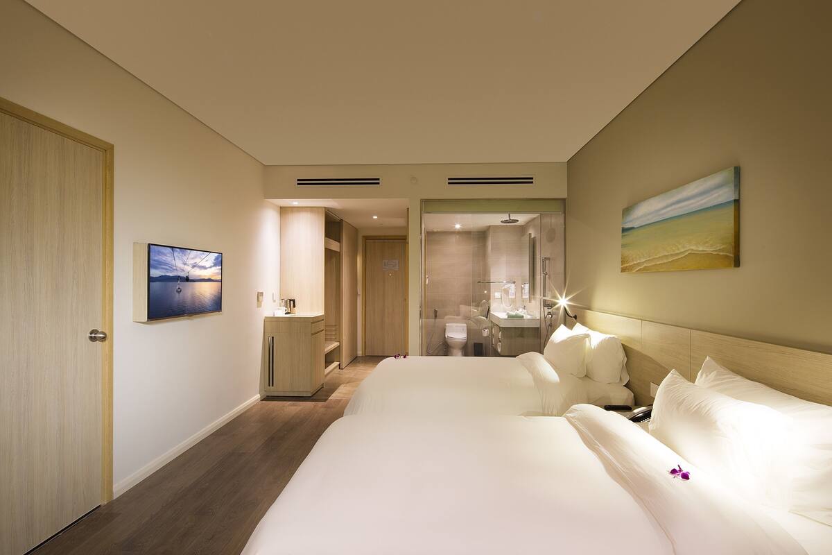 A hotel room with a large bed, a bathroom with a glass shower, and a view of the beach.