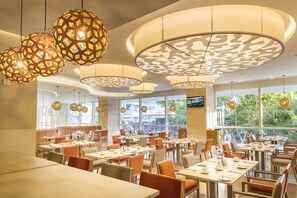 Un restaurant moderne avec des tables rondes, des chaises orange et des luminaires décoratifs suspendus au plafond.
