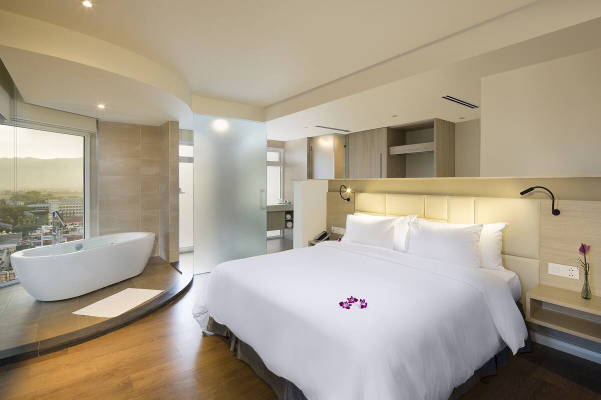 A modern hotel room with a large bed, a bathtub, and a city view.