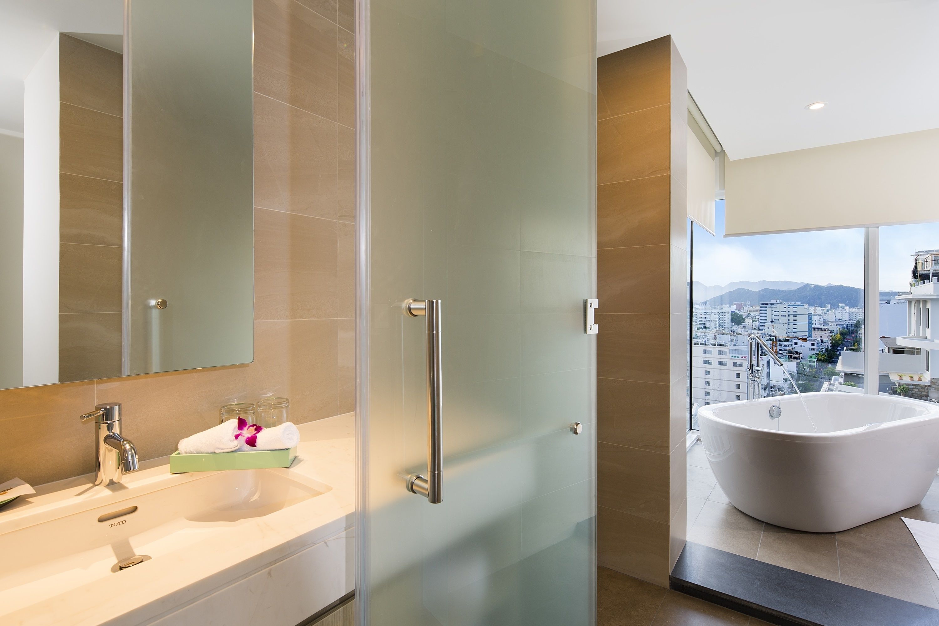 A modern bathroom with a large bathtub, a glass shower enclosure, and a city view.