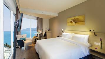 A hotel room with a large bed, a desk, a chair, and a view of the sea.