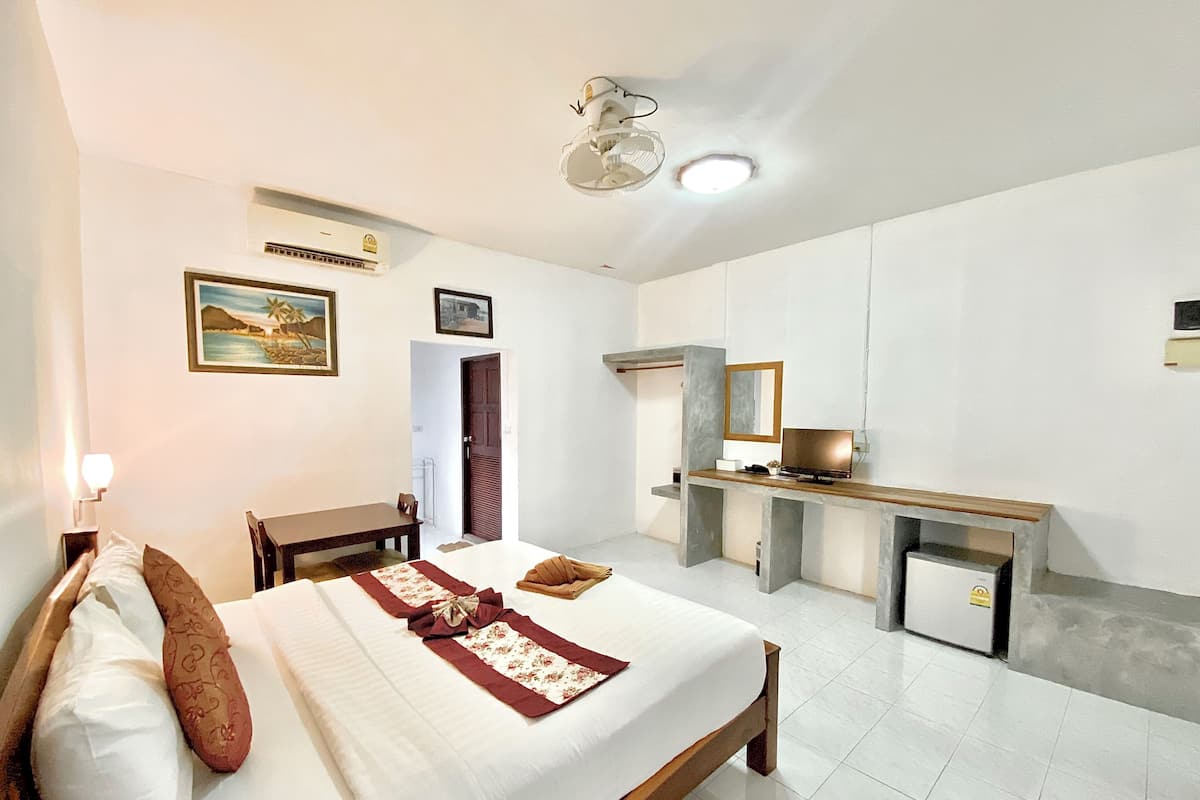 A hotel room with a bed, a desk, a chair, a small refrigerator, and a door.