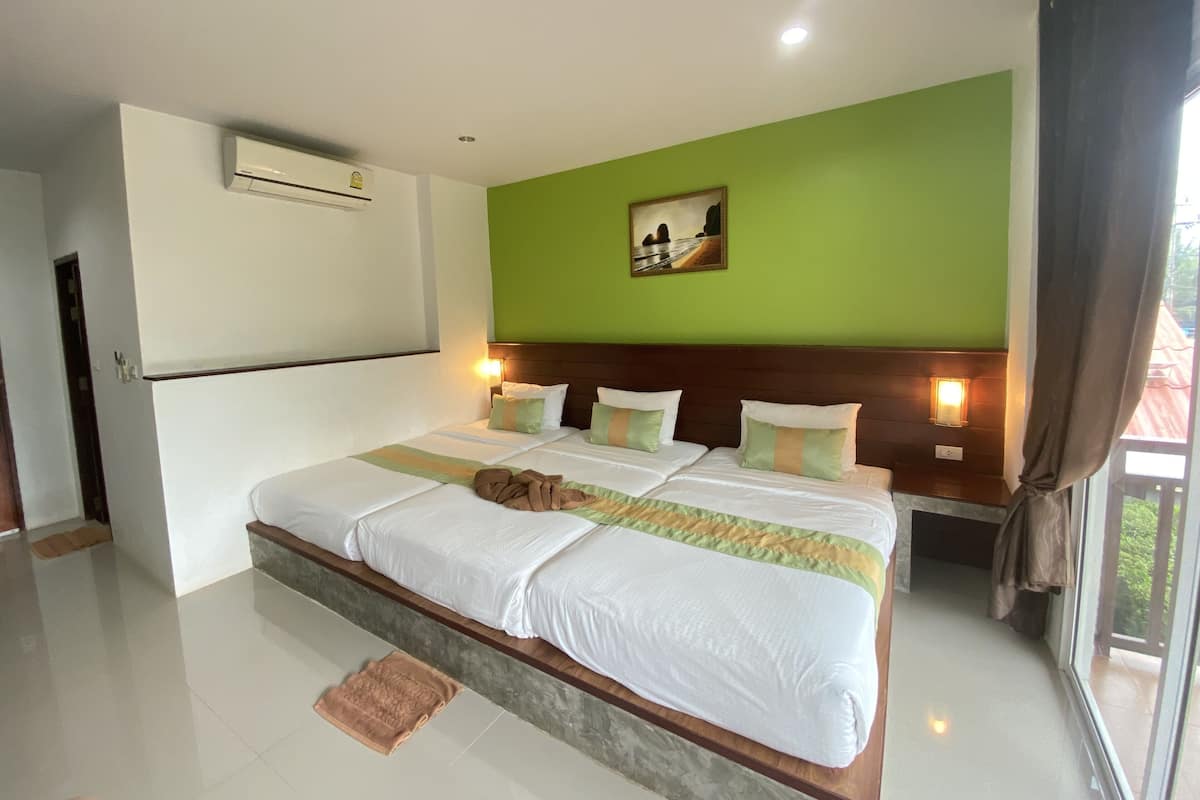 A hotel room with a large bed, green walls, a painting, and a window with curtains.