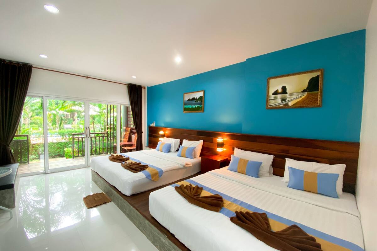 A hotel room with two beds, a balcony with a view of greenery, and a painting on the wall.